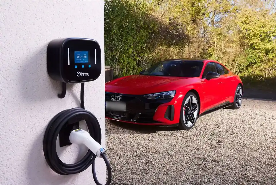 Cargador Ohme Home Pro de 7,4 kW instalado en la pared de una casa, con el cable recogido, junto a un auto eléctrico